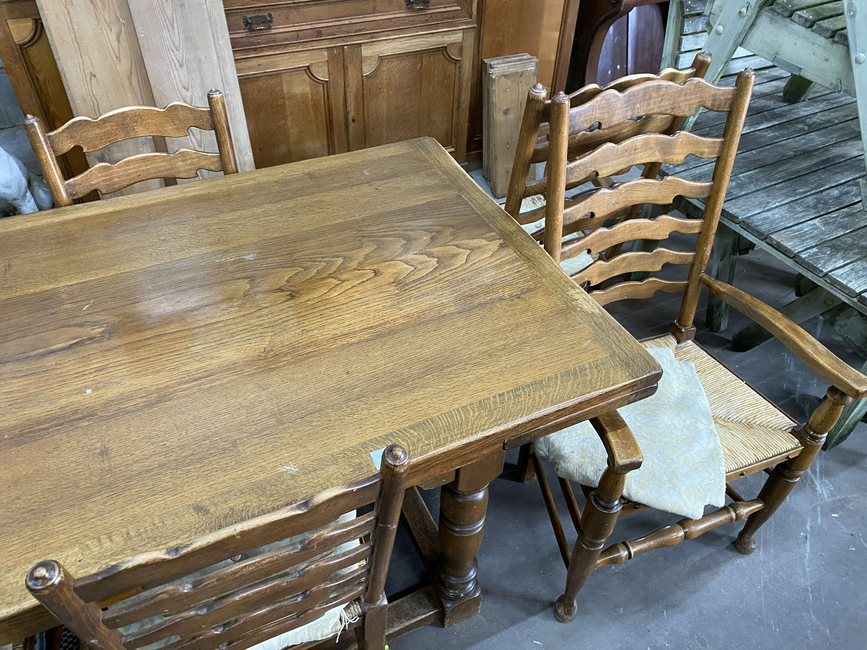 An 18th century style oak dining suite comprising extending draw leaf refectory table, 243cm extended, width 90cm, height 76cm, six rush seat ladder back chairs, two with arms and a linenfold moulded sideboard